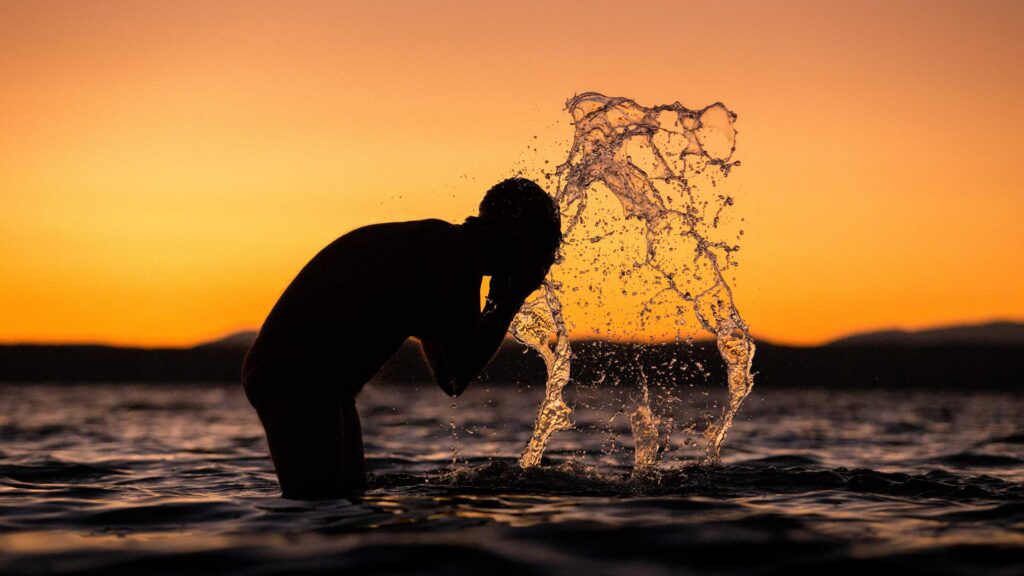 silhouette of man washing his face on body of water