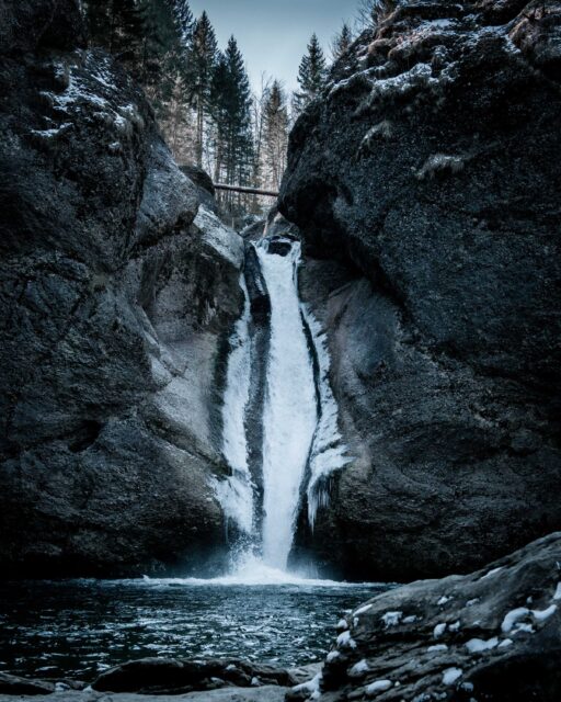 water falls between rocky mountain during daytime