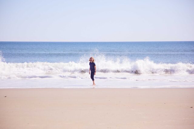woman in black dress walking on beach during daytime