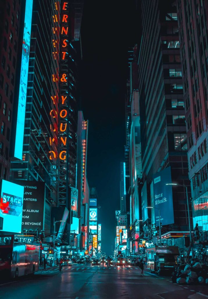 street photography of vehicles traveling on road between large buildings during nighttime